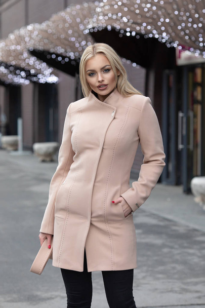 Beautiful young stylish blonde woman wearing coat walking through the city streets. Trendy casual outfit. Street fashion - Fotó, kép