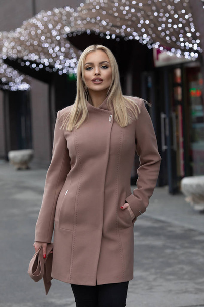 Beautiful young stylish blonde woman wearing coat walking through the city streets. Trendy casual outfit. Street fashion - Photo, Image