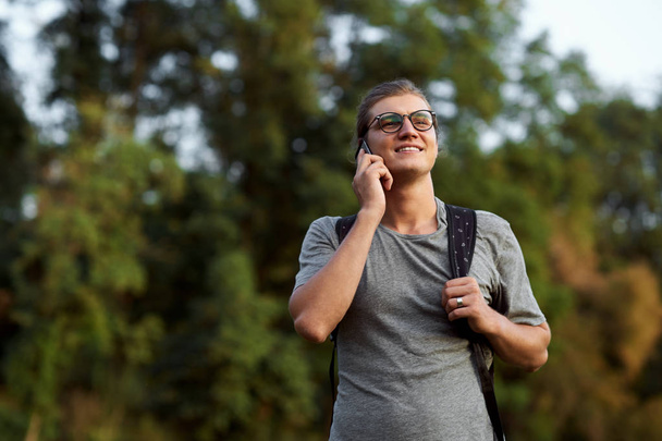 Νεαρός φοιτητής Καυκάσιος χρησιμοποιώντας κινητό τηλέφωνο έξω από το δημόσιο πάρκο. - Φωτογραφία, εικόνα