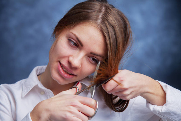 Young beautiful woman cutting with shears her long red hair. Hai - Фото, изображение