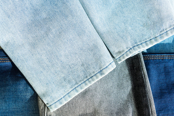 Bottom of light blue jeans lying on many other different jeans. Stack of different colored pants. Copy space. - Photo, Image