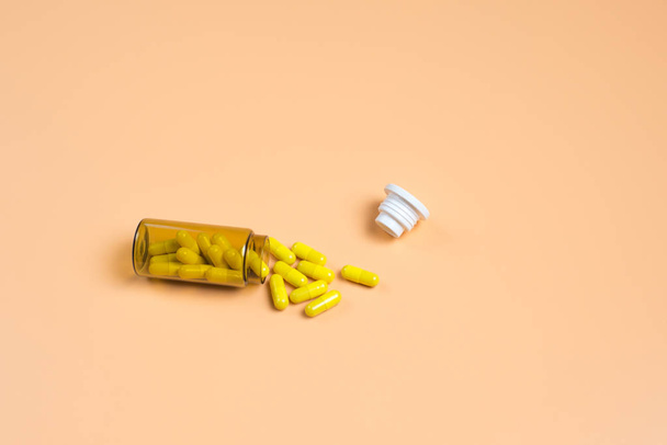 Κίτρινο χάπια σε σκοτεινόχρωμη φιάλη σε πορτοκαλί φόντο - Φωτογραφία, εικόνα