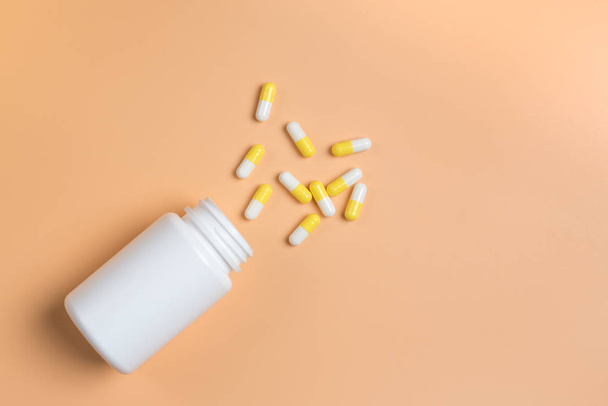 Κίτρινα και λευκά χάπια, ταμπλέτες και άσπρο μπουκάλι σε πορτοκαλί φόντο. - Φωτογραφία, εικόνα