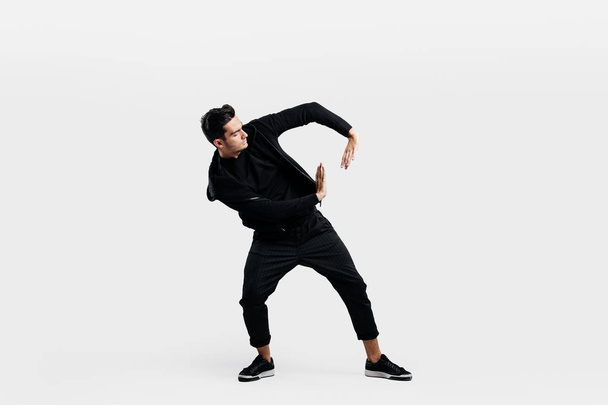 Handsome man dressed in a stylish black clothes is dancing street dance. He makes stylized movements with his hands - Foto, Imagem