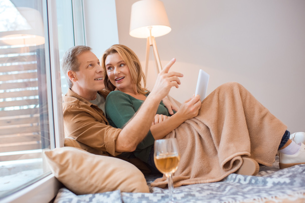 улыбающийся мужчина указывая пальцем во время использования цифрового планшета вместе с женой
 - Фото, изображение