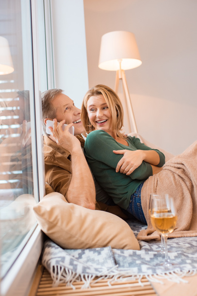 笑みを浮かべて男の妻と床に座ってスマート フォンで話す - 写真・画像