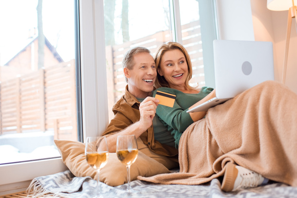 casal alegre usando laptop enquanto marido segurando cartão de crédito
 - Foto, Imagem
