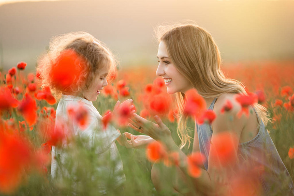 Kaunis hymyilevä lapsi tyttö nuori äiti on hauskaa alalla unikko kukkia auringonlaskun valot
 - Valokuva, kuva