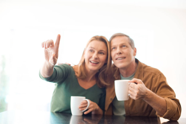 επιλεκτική εστίαση του ζεύγους που κατέχουν φλιτζάνια καφέ ενώ γυναίκα δείχνοντας με το δάχτυλο - Φωτογραφία, εικόνα