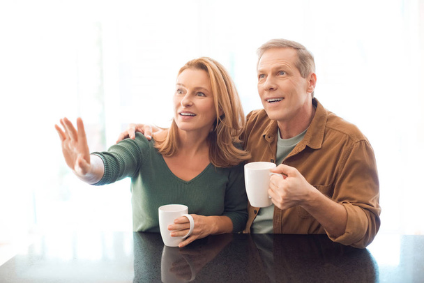 enfoque selectivo de pareja sosteniendo tazas de café mientras que la mujer señala con la mano
  - Foto, Imagen
