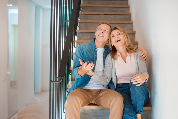 onnellinen pari syleilee istuessaan portaissa uudessa kodissa
 - Valokuva, kuva