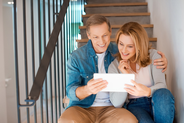 Lächelndes Paar mit digitalem Tablet, während es mit Frau auf Treppe sitzt - Foto, Bild