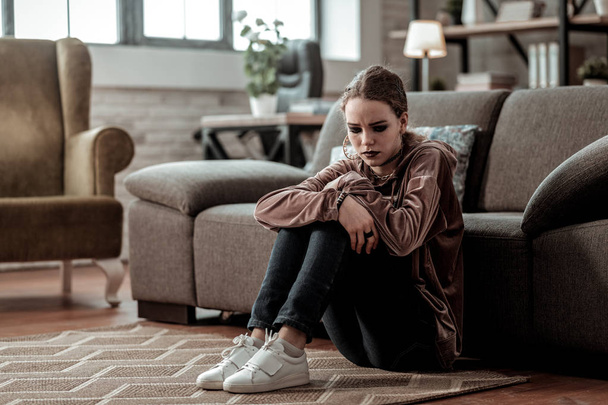Teenage girl wearing white sneakers sitting on the floor feeling stressed - Фото, изображение