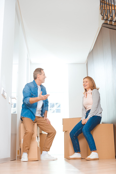 happy couple talking while sitting on cardboard boxes at new home - Fotografie, Obrázek