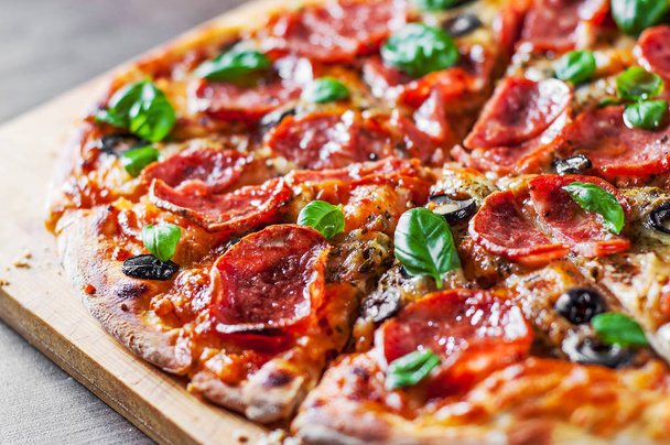 Pepperoni Pizza with Mozzarella cheese, salami, Tomatoes, olive, pepper, Spices and Fresh Basil. Italian pizza on wooden table background - Foto, Imagem