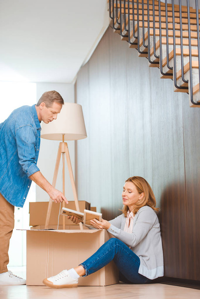 woman sitting on floor and unpacking cardboard box and man pointing with finger - Photo, Image