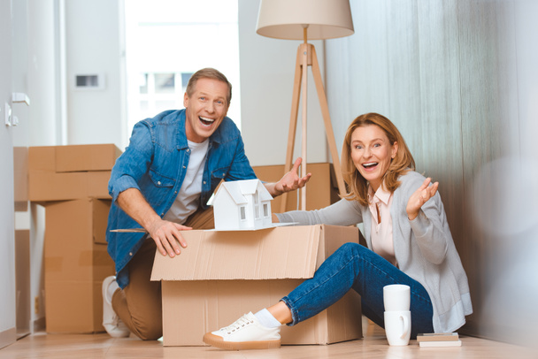 pareja feliz emocionada mostrando modelo de casa mientras desempaca la caja de cartón
 - Foto, Imagen