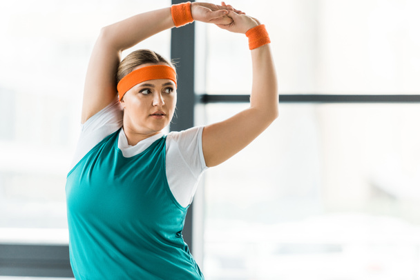 overweight woman stretching while standing in sportswear in gym - Photo, Image