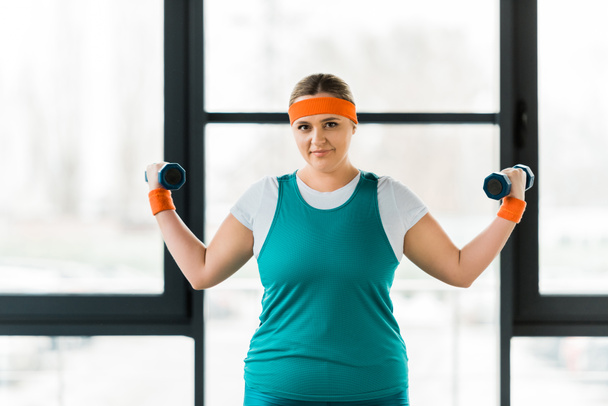 vrolijke overgewicht vrouw workouting in sportkleding met halters - Foto, afbeelding