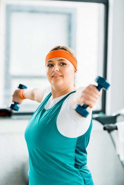 selective focus of cheerful overweight woman workouting in sportswear with dumbbells - Zdjęcie, obraz