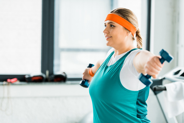 selective focus of happy overweight woman workouting in sportswear with dumbbells - Photo, Image