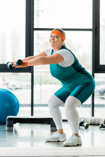 happy plus size woman exercising with dumbbells in gym - Photo, Image