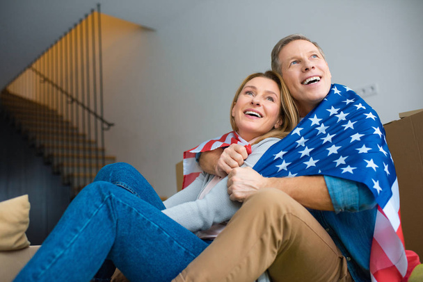 happy couple looking up while wrapping in usa national flag  - Fotoğraf, Görsel