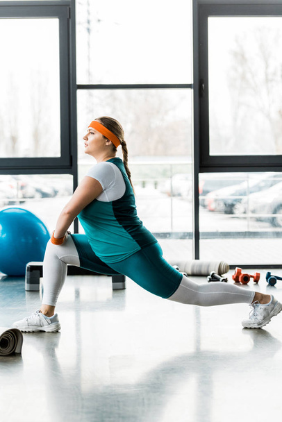 confident plus size woman in sportswear stretching in gym - Fotó, kép