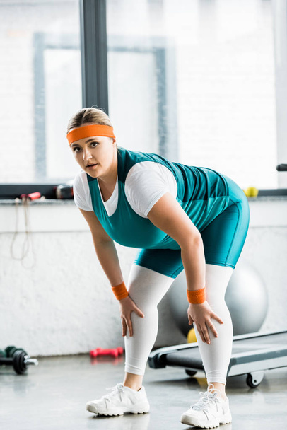 plus size girl in sportswear stretching and looking at camera in gym - Foto, Imagem