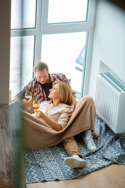 feliz pareja con copas de vino blanco descansando en el suelo por una gran ventana en el nuevo hogar
 - Foto, Imagen