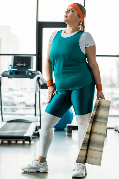 attractive overweight woman holding fitness mat in gym - Foto, afbeelding