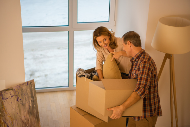 муж держит картонную коробку, а улыбающаяся женщина распаковывает коробку
 - Фото, изображение