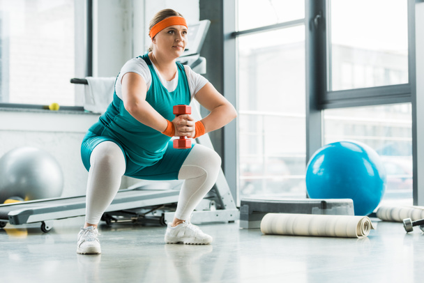 happy overweight girl squatting with dumbbell in gym - Foto, Imagem