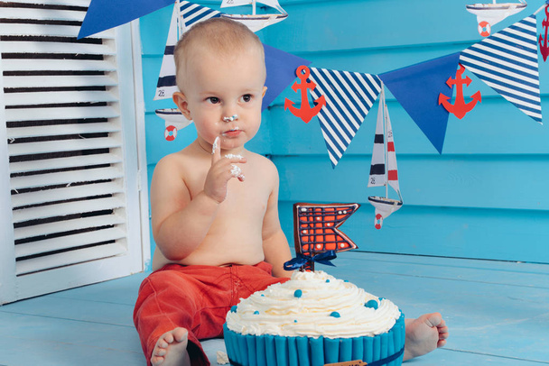 decoration for the boys birthday, smash the cake in a nautical marine style. stylized birthday ship photo shoot. Cheerful boy eats and break a cake with his hands on the first holiday - Photo, Image
