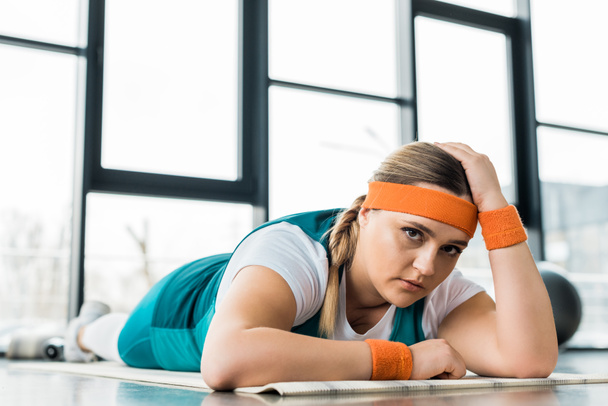 sad overweight girl lying on fitness mat in gym - Zdjęcie, obraz