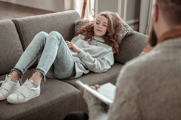 Chica usando sudadera gris escalofriante en el sofá y hablando con el consejero
 - Foto, Imagen