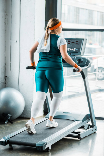 overweight girl with towel on shoulders running on treadmill in gym - Photo, Image