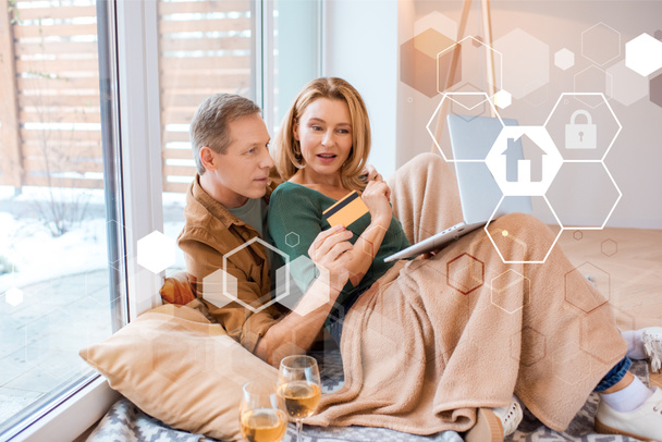 happy husband holding credit card while using laptop together with wife, smart home concept - Foto, afbeelding