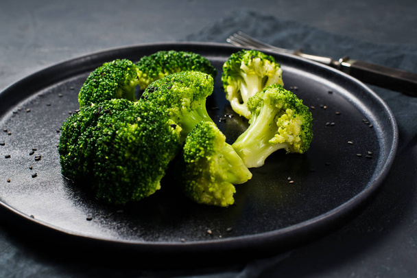 Boiled broccoli on a black plate. Black background, side view, close-up - Zdjęcie, obraz
