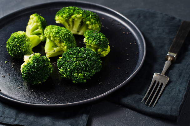 Raw broccoli on a black plate. Black background, side view, close-up - Photo, Image