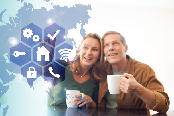 selective focus of amused happy couple holding coffee cups, smart home concept - Photo, Image