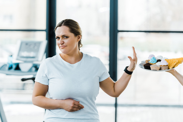 περικοπεί θεώρηση του ανθρώπου πλατώ με νόστιμα ζαχαροπλαστείο κοντά υπέρβαρη γυναίκα δείχνει κανένα σημάδι - Φωτογραφία, εικόνα