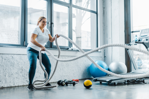 весела зайва вага жінка тренується з бойовими мотузками в тренажерному залі
 - Фото, зображення
