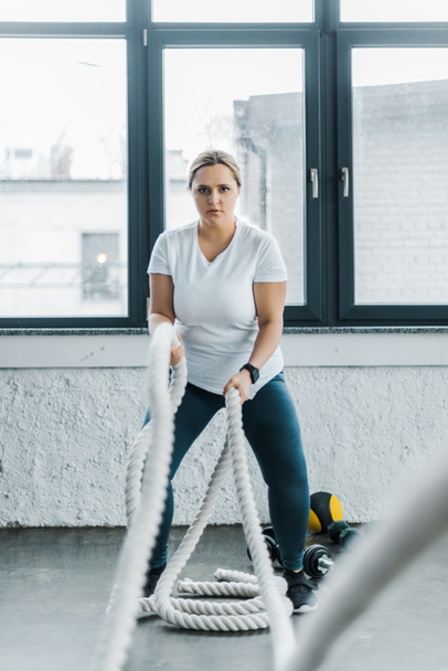 treinamento mulher plus size concentrado com cordas de batalha no ginásio
 - Foto, Imagem