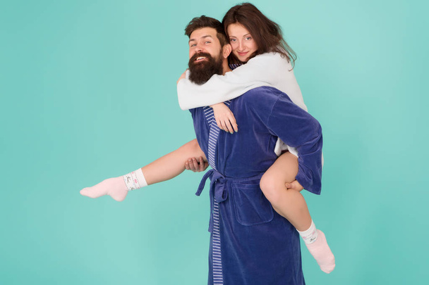 Lets stay at home and have fun. Couple in bathrobes having fun turquoise background. They always have fun together. Close relationship. Handsome young man giving his girlfriend piggyback ride - Fotografie, Obrázek
