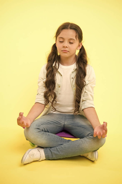 Little girl meditate sitting on penny board on yellow background. Time for yoga. Hipster child activity. Concentration and meditation. Staying calm. Skating is her life.Relaxation exercise - Foto, immagini