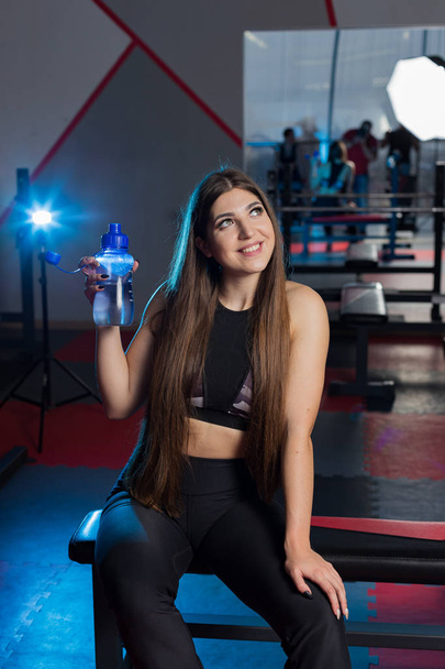 Piękne seksowne fitness model odpoczynek po treningu na ławce z butelką wody w parze w siłowni. - Zdjęcie, obraz