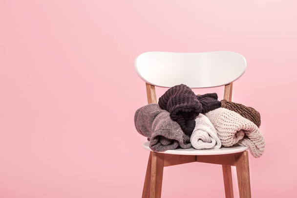 White chair with a stack of knitted sweaters on a pink backgroun - Photo, Image