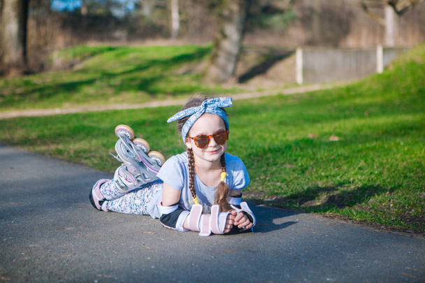 Menina encaracolado bonito engraçado deitado em patins de rolo e olhando para a câmera
. - Foto, Imagem