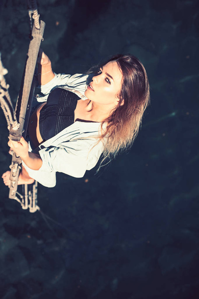 She is entirely dominated by ambition. Pretty woman climb jacobs ladder to the top. Sexy woman climbing up rope ladder. Sensual woman hang on rope over water surface. Achieving her towering ambition - Photo, Image